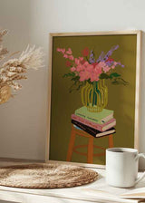 Cuadro con jarrón rayado amarillo y verde, flores rosadas y lilas, libros apilados sobre taburete de madera, fondo ocre, estilo ilustración. Disponible en kudeko.com