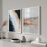 Conjunto de dois quadros abstratos emoldurados com formas etéreas em branco, cinzento, preto e detalhes dourados, composição contemporânea com textura mineral e horizontes difusos. Disponível em kudeko.com