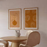Cuadro con hojas tropicales monstera en contornos blancos sobre fondo terracota cálido, composición botánica limpia de estilo minimalista. Disponible en kudeko.com