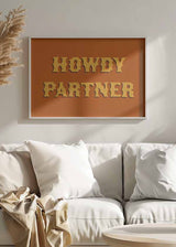 Quadro horizontal com a frase Howdy Partner, letras amarelas grandes, fundo laranja e composição tipográfica de estilo western retro para decoração de parede. Disponível em kudeko.com