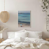 Quadro de praia mediterrânica com mar turquesa, areia clara, guarda-sol azul, duas pessoas a descansar e estilo fotográfico em tons de azul, bege e branco. Disponível em kudeko.com
