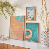 Gerahmtes Wandbild mit Schriftzug La Dolce Vita über einer Strandszene in Koralle, Türkis und Beige, mit Wellenmeer, Sand, Schwimmringen, Getränken und mediterranem Typografie Stil. Erhältlich auf kudeko.com