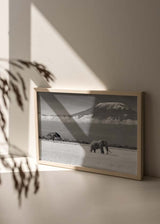 Horizontales Wandbild mit einem einzelnen Elefanten in der Savanne, schneebedecktem Berg im Hintergrund, tiefen Wolken sowie Grau-, Weiß- und Schwarztönen im fotografischen Stil. Erhältlich auf kudeko.com