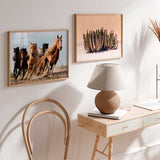 Cuadro horizontal de seis caballos corriendo sobre tierra, con polvo en movimiento, tonos marrones, negros, beige y cielo azul, en estilo fotográfico. Disponible en kudeko.com