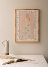 Gerahmtes Wandbild mit weiblicher Figur beim Selfie vor einem Spiegel, zartrosa Hintergrund, lilafarbenes Handy, wassergrüner Rock mit rosa Blumen, feiner Illustrationsstil und moderne Pastelltöne. Erhältlich auf kudeko.com