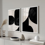 Quadro emoldurado abstrato com grandes formas orgânicas pretas sobre fundo bege claro, composição limpa em tons neutros e estilo contemporâneo. Disponível em kudeko.com