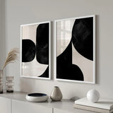 Conjunto de dos cuadros con formas abstractas curvas en negro intenso sobre fondo beige claro, composición moderna de alto contraste y estilo abstracto. Disponible en kudeko.com