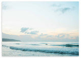 Quadro horizontal de mar calmo ao amanhecer com ondas suaves, céu claro, nuvens difusas, silhueta ao longe, tons azul-claro, bege e branco, estilo fotográfico. Disponível em kudeko.com