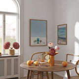 Cuadro de puerta azul turquesa en fachada blanca con macetas simétricas, bicicleta ligera, cielo azul claro y estilo fotográfico mediterráneo. Disponible en kudeko.com