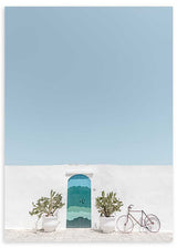 Cuadro de puerta azul turquesa en fachada blanca con macetas simétricas, bicicleta ligera, cielo azul claro y estilo fotográfico mediterráneo. Disponible en kudeko.com