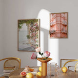 Cuadro de fachada clásica rosa pastel con balcones de hierro, ventanas arqueadas y detalles ornamentales, de estilo fotográfico. Disponible en kudeko.com
