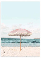 Cuadro de sombrilla rosa con flecos sobre playa de arena clara, mar azul sereno y cielo pastel, en estilo fotográfico. Disponible en kudeko.com
