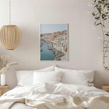 Quadro de porto costeiro com casas em tons pastel, barcos atracados, passeio junto ao mar, água azul esverdeada e estilo fotográfico mediterrânico. Disponível em kudeko.com