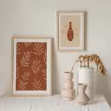 Cuadro con ramas de hojas en líneas color crema sobre fondo terracota cálido, composición botánica repetitiva de estilo floral. Disponible en kudeko.com
