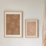 Cuadro con hojas botánicas finas y ramas delineadas en beige sobre fondo terracota cálido, de estilo floral. Disponible en kudeko.com
