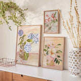Cuadro de hortensias azul lavanda y blancas en jarrón de cristal, con hojas verdes, fondo beige rosado y estilo floral. Disponible en kudeko.com