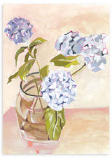 Cuadro de hortensias azul lavanda y blancas en jarrón de cristal, con hojas verdes, fondo beige rosado y estilo floral. Disponible en kudeko.com