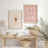 Cuadro con frase LOVE LIVES HERE en letras blancas grandes sobre fondo rosa empolvado, composición tipográfica elegante de estilo con frases. Disponible en kudeko.com