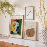 Quadro com retrato feminino cubista, boina vermelha, cabelo amarelo, rosto em tons azulados, fundo verde e rosa, estilo de ilustração com linhas marcadas e composição artística. Disponível em kudeko.com