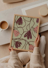 Tableau encadré avec fleurs retombantes en bordeaux, rose poudré et brun sur fond vert doux, composition organique au style floral épuré. Disponible sur kudeko.com