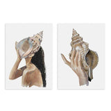 Conjunto de dois quadros emoldurados com mulher e mão a segurar uma grande concha, em tons areia, bege, creme, castanho suave e preto, estilo ilustração sobre fundo branco. Disponível em kudeko.com