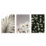 Conjunto de tres cuadros con hoja de palma, flores blancas y flores silvestres sobre fondo verde. Disponible en kudeko.com.