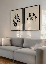 Conjunto de dois quadros com ramos de folhas pretas e flores silvestres pretas sobre fundo bege, composição botânica minimalista de linhas simples e estilo contemporâneo. Disponível em kudeko.com