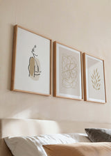 Conjunto de três quadros com linhas abstratas bege, silhueta feminina de traço contínuo, folhas decorativas em tons de areia e estilo minimalista para parede. Disponível em kudeko.com