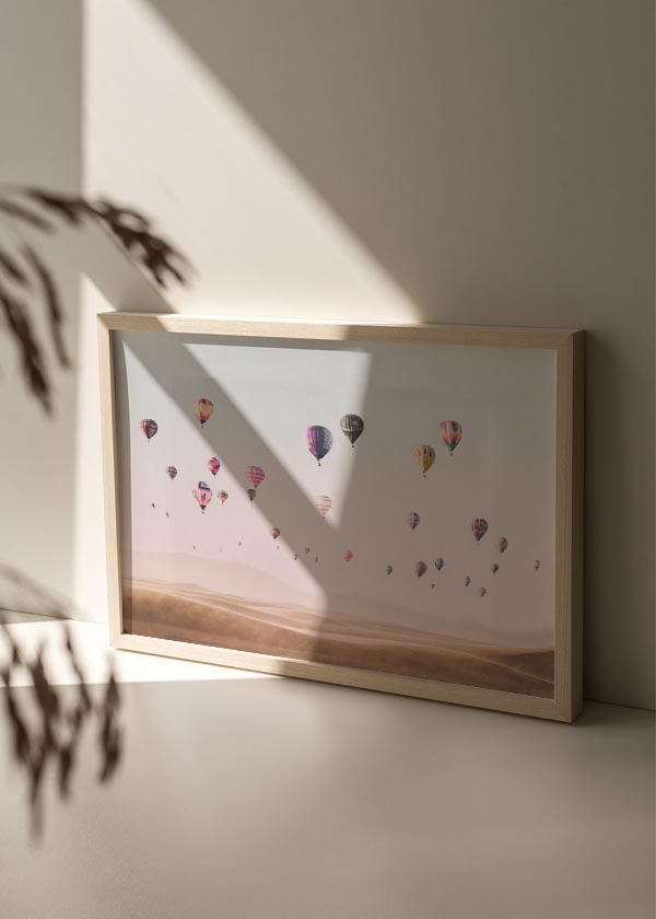 Cuadro horizontal de globos aerostáticos sobre dunas desérticas en tonos rosa, beige arena, malva y detalles multicolor, de estilo fotográfico. Disponible en kudeko.com