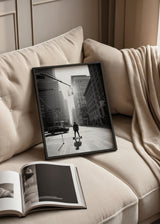 Wandbild einer städtischen Avenue in Manhattan mit hohen Wolkenkratzern, Figur auf Skateboard, hängender Ampel, Gegenlicht, Schwarz-Weiß-Tönen und fotografischem zeitgenössischem Stil. Erhältlich auf kudeko.com
