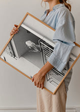 Tableau d’une femme sur le balcon d’un immeuble urbain, en noir et blanc, avec rambardes métalliques, scène du quotidien et style photographique moderne. Disponible sur kudeko.com