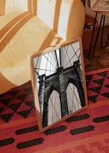Tableau du pont de Brooklyn en noir et blanc, avec arches en pierre, câbles tendus, perspective basse, composition symétrique et style photographique urbain architectural. Disponible sur kudeko.com
