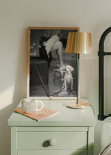 Quadro emoldurado com pequeno cão sentado junto a alpercatas, cena de interior a preto e branco, tons neutros e estilo fotográfico intimista. Disponível em kudeko.com