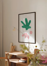 Gerahmtes Wandbild mit abstrakten organischen Formen in Grün und sanftem Rosa auf weißem Hintergrund, zentraler Silhouette, kleinem Kreis und offenen Linien im minimalistischen Stil. Erhältlich auf kudeko.com