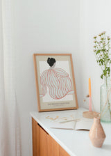 Gerahmtes Wandbild mit weiblicher Rückenfigur von hinten, korallfarben gestreiftem Pullover, beigem und weißem Hintergrund, weichen Linien und reduziertem illustrativem Stil. Erhältlich auf kudeko.com