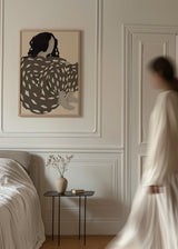Quadro emoldurado com figura feminina de costas, cabelo escuro, vestido cinzento taupe com detalhes claros, fundo bege e estilo de ilustração sereno e simples. Disponível em kudeko.com
