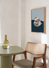 Tableau encadré avec femme allongée sur un lit dans une tasse à café blanche, fond bleu clair, table bleu marine et style vintage délicat. Disponible sur kudeko.com