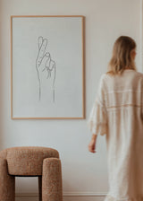 Gerahmtes Wandbild mit Hand und gekreuzten Fingern in feinen schwarzen Linien, auf strukturiertem beigem Hintergrund, im minimalistischen und zeitgenössischen Stil mit ruhigen Naturtönen. Erhältlich auf kudeko.com