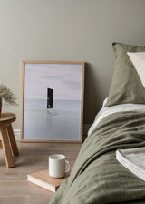 Tableau encadré avec porte noire ouverte, escalier blanc sur mer calme, ciel gris perle et bleu pâle, silhouette humaine partielle, style minimaliste contemplatif. Disponible sur kudeko.com