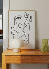 Gerahmtes Wandbild mit weiblichem Gesicht als Linienzeichnung, zarten Blumen, weißem Hintergrund, klaren schwarzen Linien und elegantem minimalistischem Stil. Erhältlich auf kudeko.com