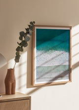 Quadro com vista aérea do mar e da costa, água turquesa, espuma branca, areia bege suave e estilo fotográfico sereno. Disponível em kudeko.com