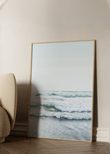 Gerahmtes Wandbild mit Meeresmotiv, sanften Wellen am Ufer, weißem Schaum, blaugrünem Wasser, nassem Sand und ruhigem fotografischem Stil. Erhältlich auf kudeko.com