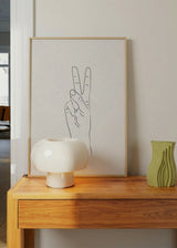 Gerahmtes Wandbild mit Hand als Friedenszeichen, feinen schwarzen Linien, hellbeigem Hintergrund, minimalistischer Stilrichtung und klarer Komposition für moderne Wohnräume. Erhältlich auf kudeko.com