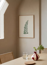 Tableau encadré avec branche stylisée de feuilles allongées vert sauge et vert grisé sur fond blanc, composition épurée au style minimaliste et élégant. Disponible sur kudeko.com