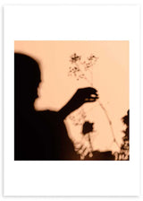 Quadro com silhueta feminina sombreada a segurar flores silvestres, fundo bege quente, contraste preto e estilo fotográfico poético. Disponível em kudeko.com