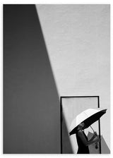 Wandbild mit Schwarz-Weiß-Fotografie einer Frau mit weißem Regenschirm neben einer Tür, diagonaler Lichtführung, markantem Schatten an der Wand und sachlichem fotografischem Stil. Erhältlich auf kudeko.com