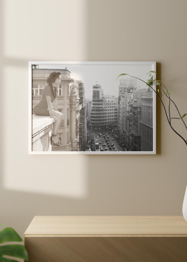 Horizontales Wandbild mit einer Frau auf einer Gesimskante vor städtischer Allee, klassischen Gebäuden, Schwarz-Weiß-Tönen und zeitgenössischem Stadtstil. Erhältlich auf kudeko.com