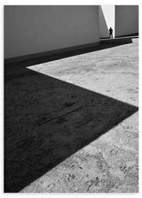 Quadro de cena arquitetónica a preto e branco com sombras diagonais, chão de betão texturado, figura humana distante e estilo fotográfico contemporâneo. Disponível em kudeko.com