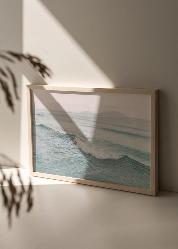 Cuadro horizontal de olas suaves en mar azul verdoso con espuma blanca, horizonte brumoso, montañas lejanas y estilo fotográfico sereno. Disponible en kudeko.com