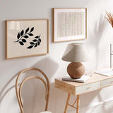 Horizontales Wandbild mit zwei schwarzen Blattzweigen auf hellbeigem Hintergrund, schlichte botanische Komposition, klare Linien, minimalistischer Stil und neutrale Farbwirkung für moderne Wandgestaltung. Erhältlich auf kudeko.com